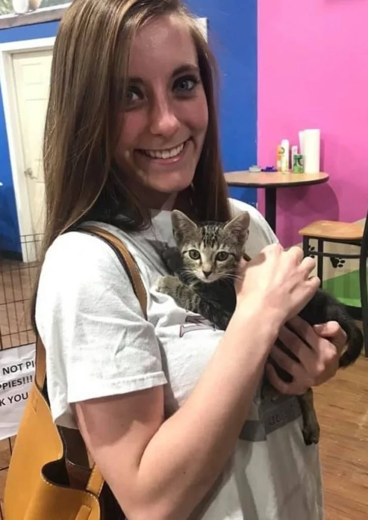 Girl holding little tabby kitten on chest in pet store