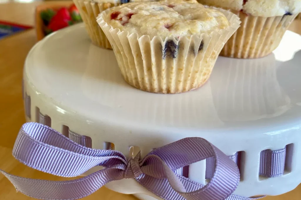 Berry muffins on top of a cake stand with a purple ribbon wrapped around it that could cause vomiting and other health issues if cats eat it